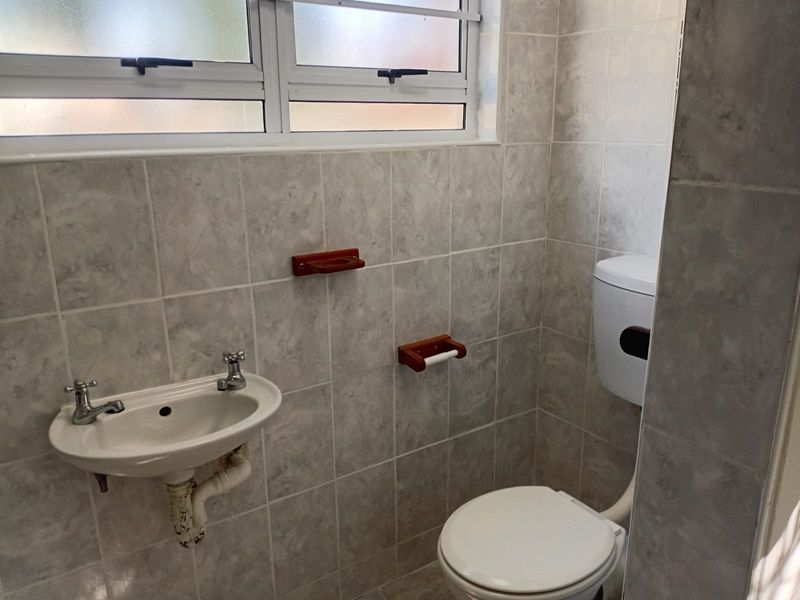A compact bathroom featuring tiled walls, a wall-mounted basin, and a standard toilet, illuminated by a frosted glass window.