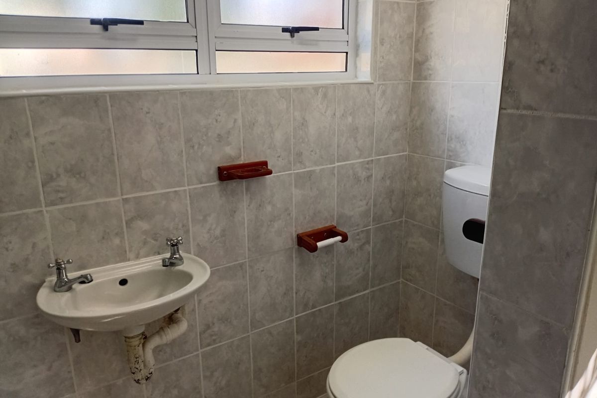 A compact bathroom featuring tiled walls, a wall-mounted basin, and a standard toilet, illuminated by a frosted glass window.