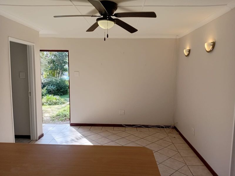 An empty living area featuring tiled flooring, a ceiling fan, and wall sconces, with direct access to the garden.