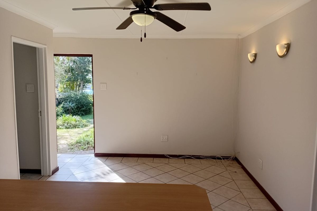 An empty living area featuring tiled flooring, a ceiling fan, and wall sconces, with direct access to the garden.
