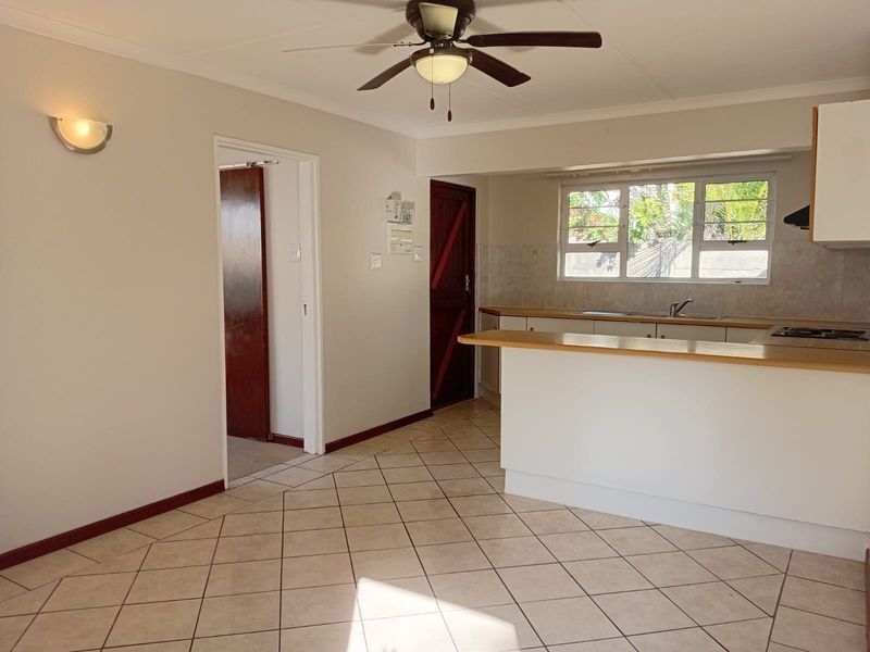 Open plan kitchen and living area featuring tiled flooring, a ceiling fan, and functional kitchen cabinetry with a breakfast counter.