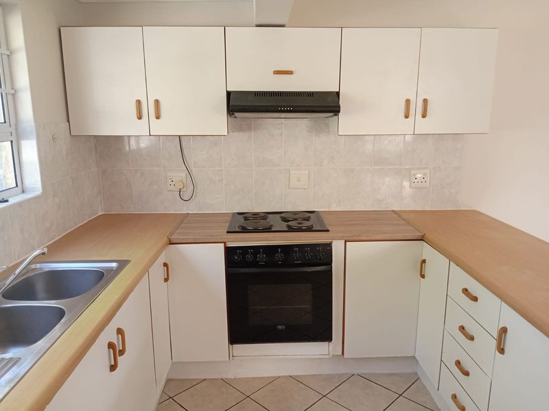 A functional kitchen featuring white cabinetry, laminate countertops, a built-in oven with hob, and a stainless steel double sink.