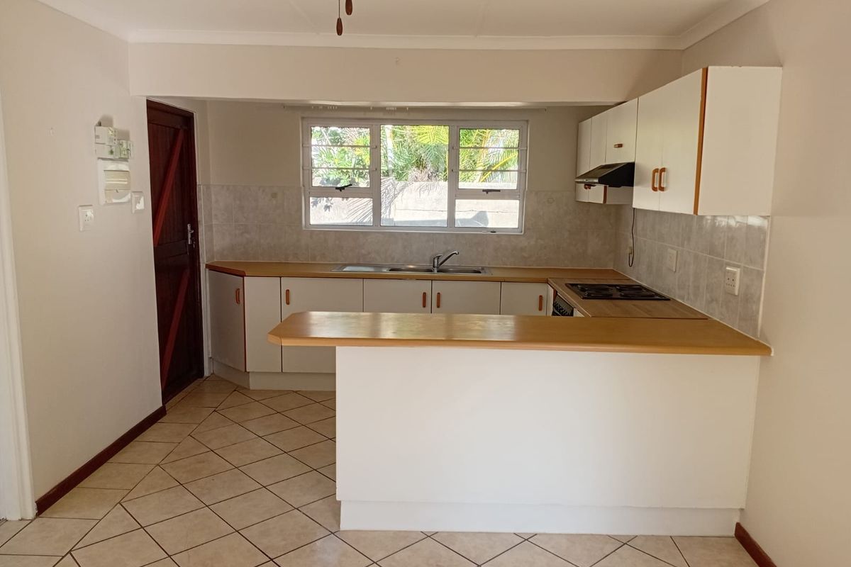 A functional kitchen featuring built-in cabinetry, laminate countertops, a built-in hob with extractor fan, and tiled flooring throughout.