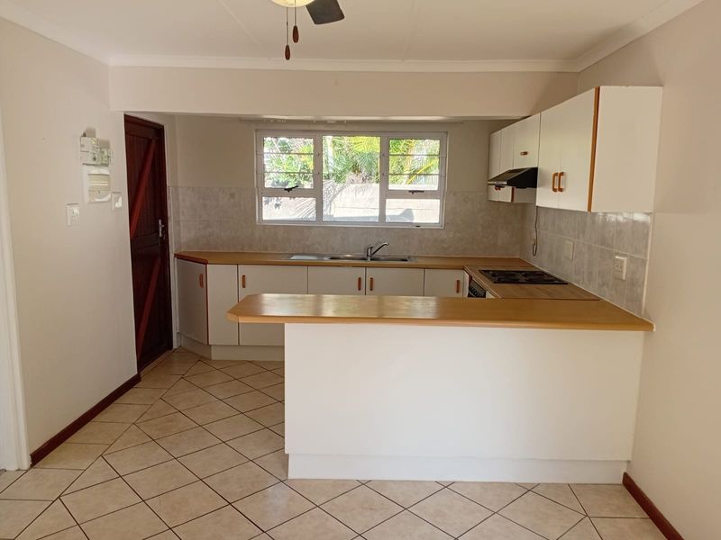 A functional kitchen featuring built-in cabinetry, laminate countertops, a built-in hob with extractor fan, and tiled flooring throughout.