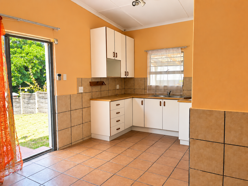 A functional kitchen featuring built-in cabinetry, tiled backsplash, and direct access to the rear garden through a sliding glass door.