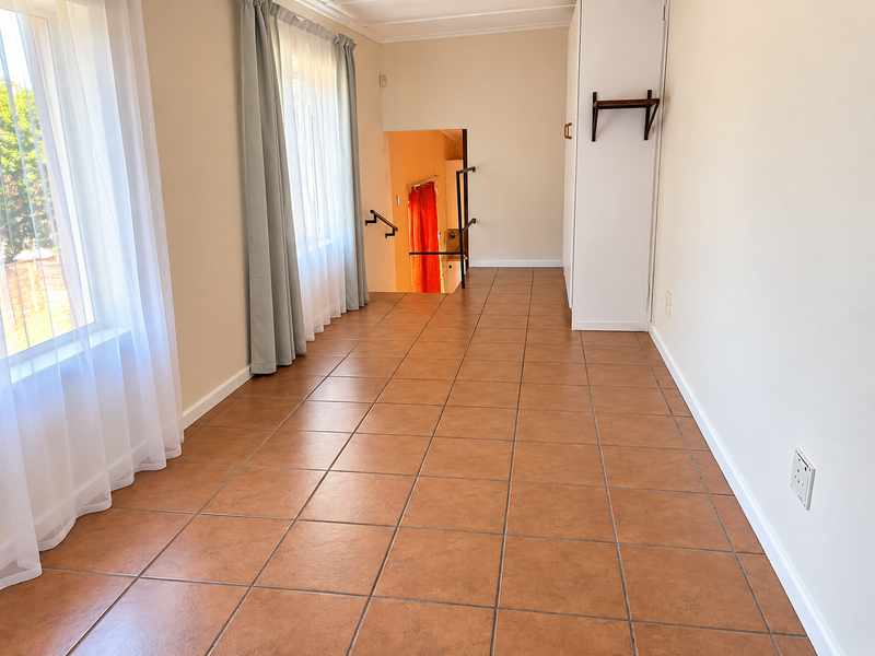 A bright, empty hallway featuring tiled flooring, built-in storage cupboards, and a staircase leading to a lower level.
