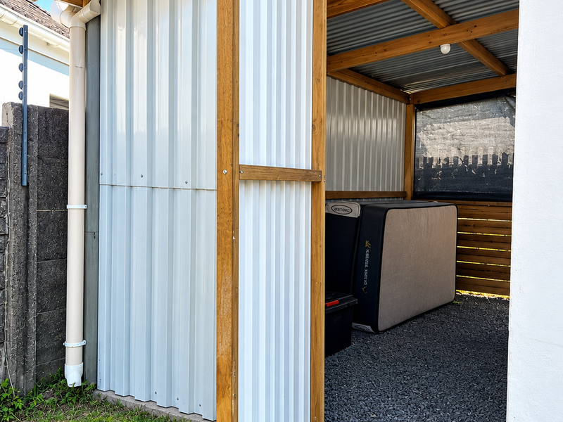 A well-constructed outdoor utility storage area featuring a timber frame, corrugated metal cladding, and gravel flooring.