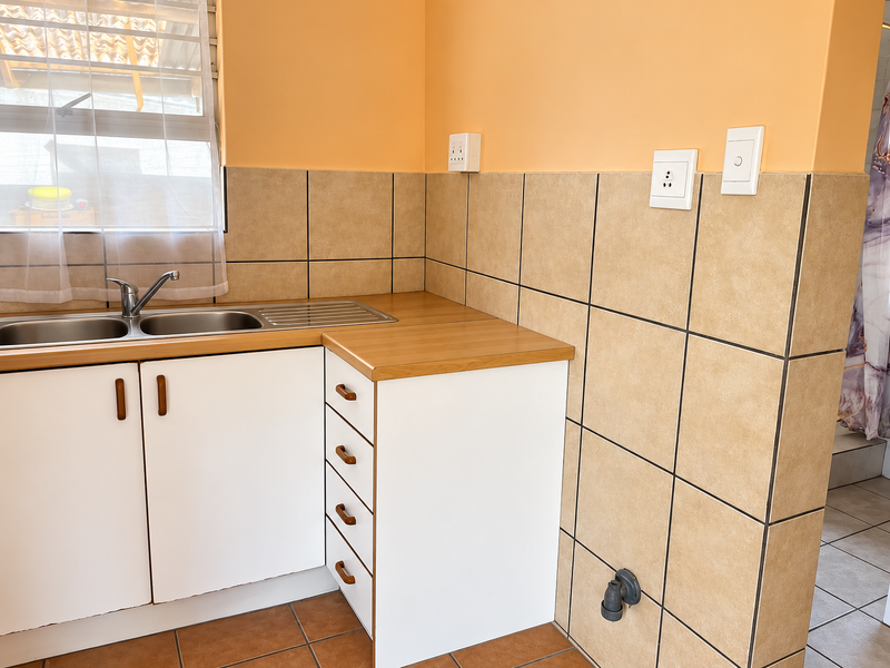 A functional kitchen area featuring white cabinetry, a stainless steel sink, laminate countertops, and neutral tiled splashbacks with integrated electrical and plumbing points.