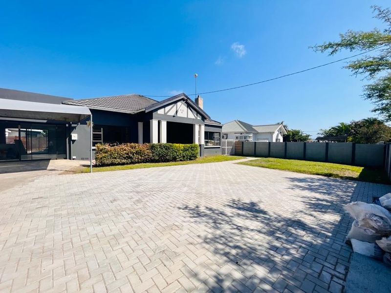 Spacious front exterior view of the property featuring a large paved driveway, covered patio area, and secure boundary walling.