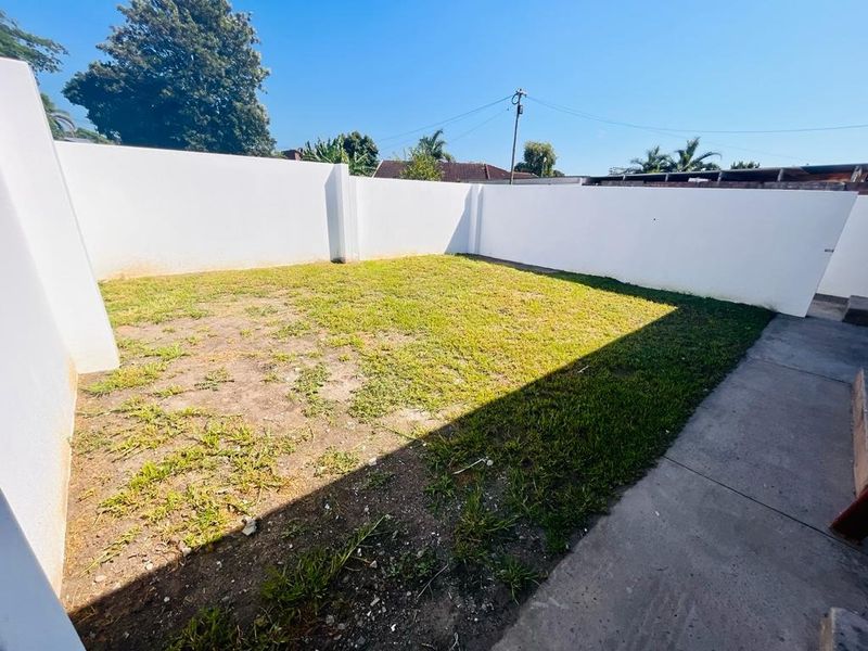 A private rear garden area featuring a concrete pathway and high perimeter boundary walls, currently requiring landscaping and lawn maintenance.