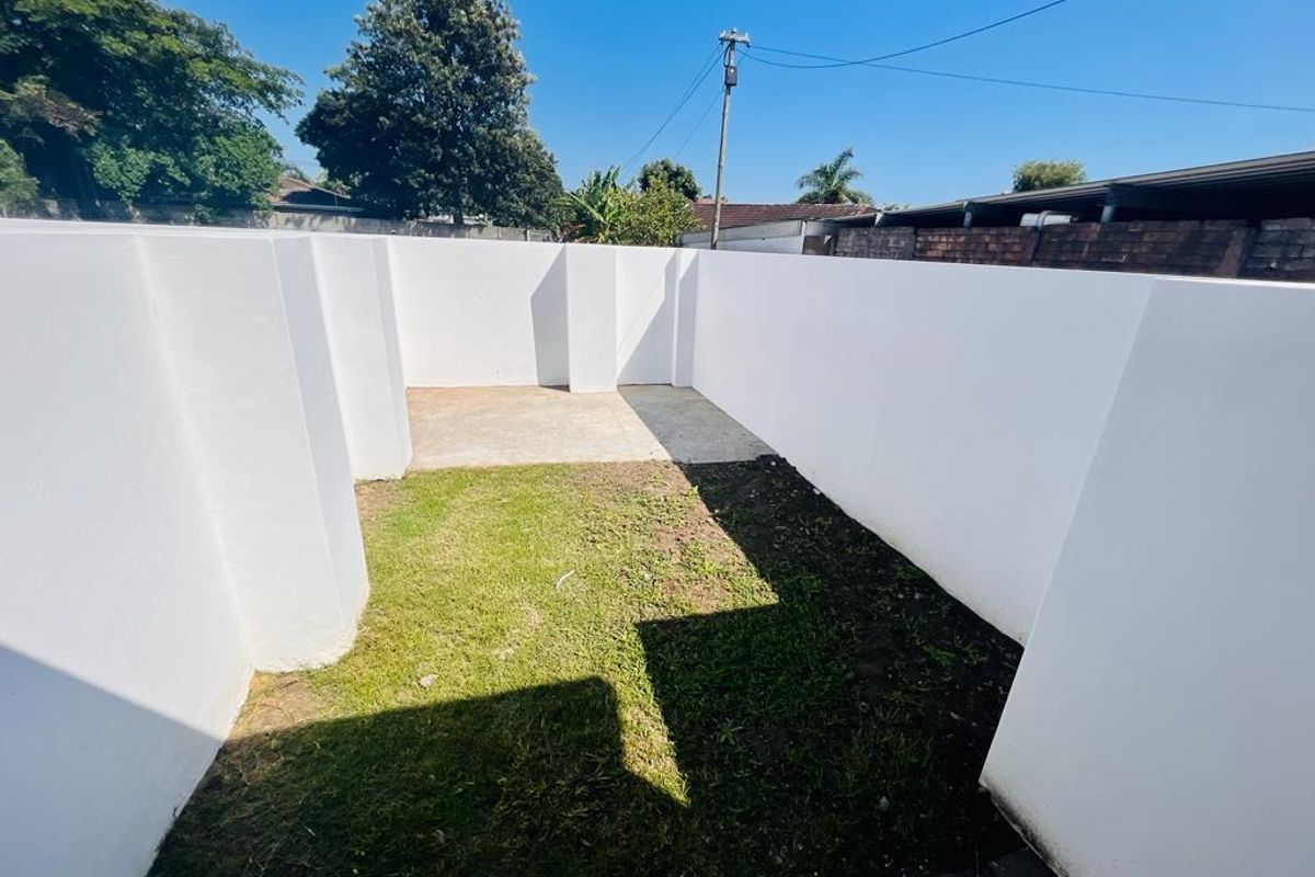 A private rear courtyard area featuring a combination of concrete paving and a small lawn section enclosed by high boundary walls.