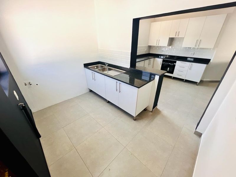 A clean, modern kitchen featuring white cabinetry, granite countertops, a double sink, and built-in appliances with a subway tile backsplash and tiled flooring.