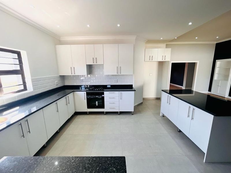 Modern kitchen featuring white cabinetry, black granite countertops, subway tile backsplash, and a central island with integrated gas hob and oven.