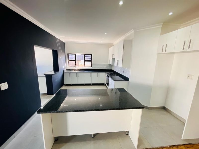 Modern kitchen featuring white cabinetry, dark granite countertops, a central island, gas hob, and tiled flooring in an open-plan layout.