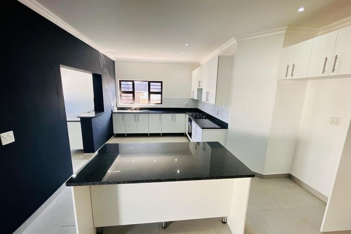 Modern kitchen featuring white cabinetry, dark granite countertops, a central island, gas hob, and tiled flooring in an open-plan layout.
