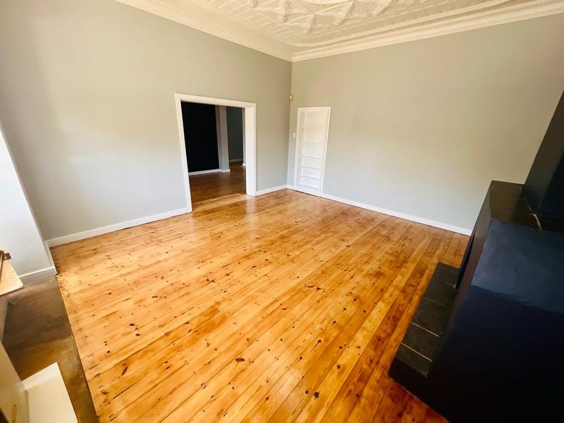 Spacious living room featuring polished hardwood flooring, an ornate ceiling, and a built-in fireplace, offering a bright and versatile living space.