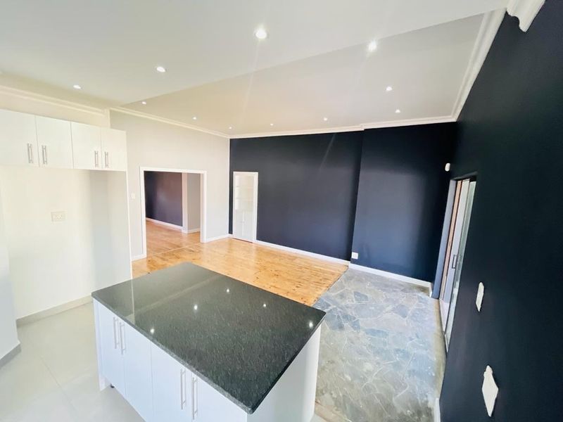 Spacious open-plan living area featuring a modern kitchen island with granite countertops, recessed lighting, and a combination of stone and hardwood flooring.