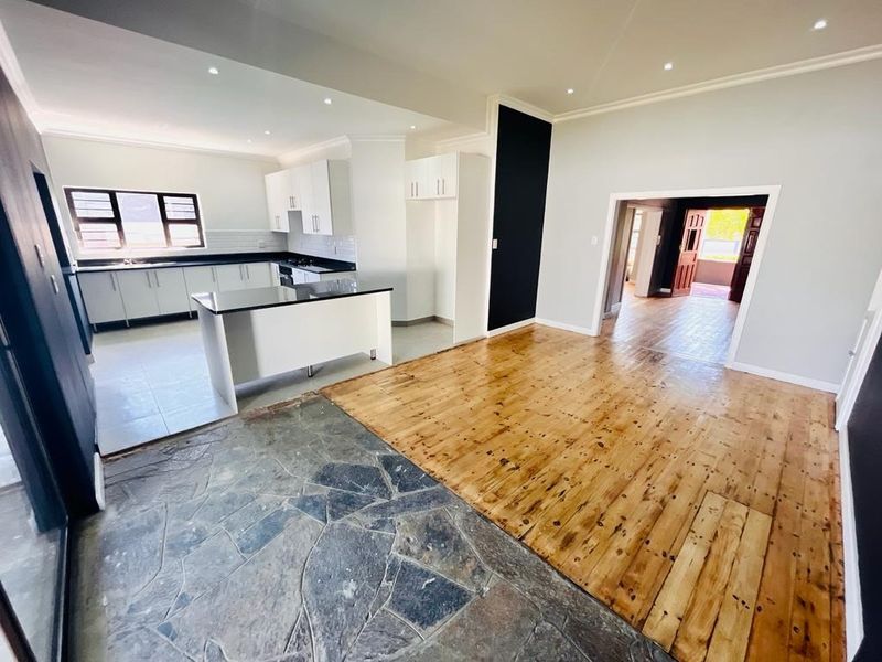 Spacious open-plan living and kitchen area featuring a modern kitchen with granite countertops, recessed lighting, and a combination of timber and stone flooring.