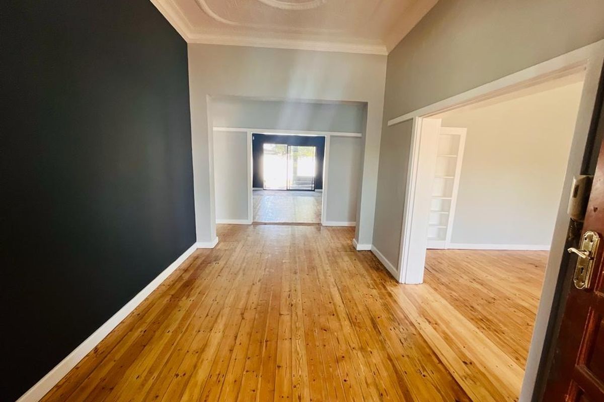 Spacious living area featuring polished hardwood flooring, ornate ceiling detailing, and large sliding glass doors providing natural light and access to the rear.