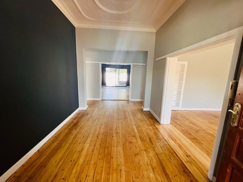 Spacious living area featuring polished hardwood flooring, ornate ceiling detailing, and large sliding glass doors providing natural light and access to the rear.