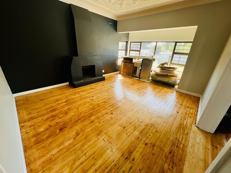 Spacious living room featuring polished hardwood floors, a prominent black fireplace, and ornate ceiling detailing, offering a bright and versatile living space.