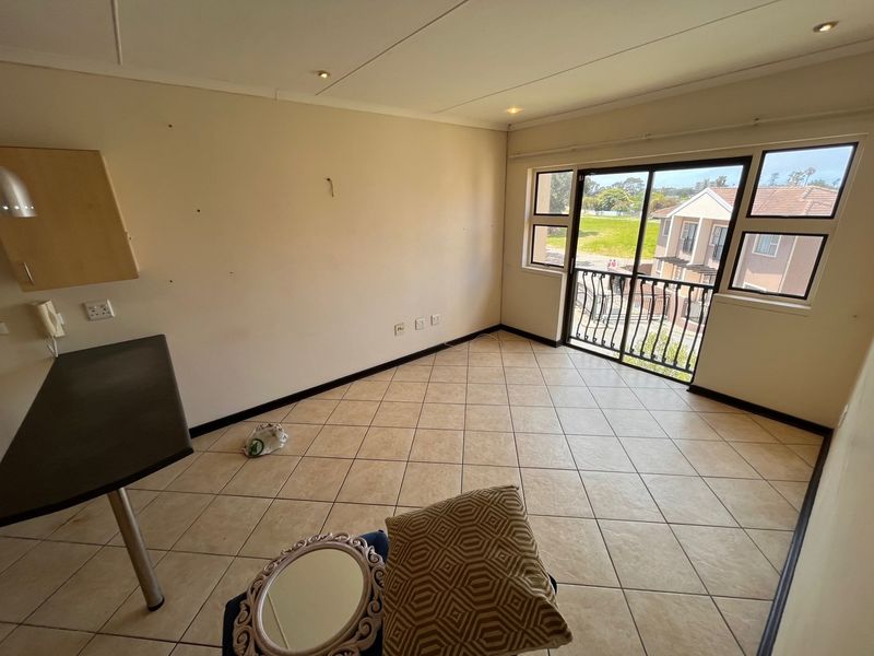 An empty living area featuring tiled flooring, recessed lighting, and a sliding glass door leading to a balcony with exterior views.