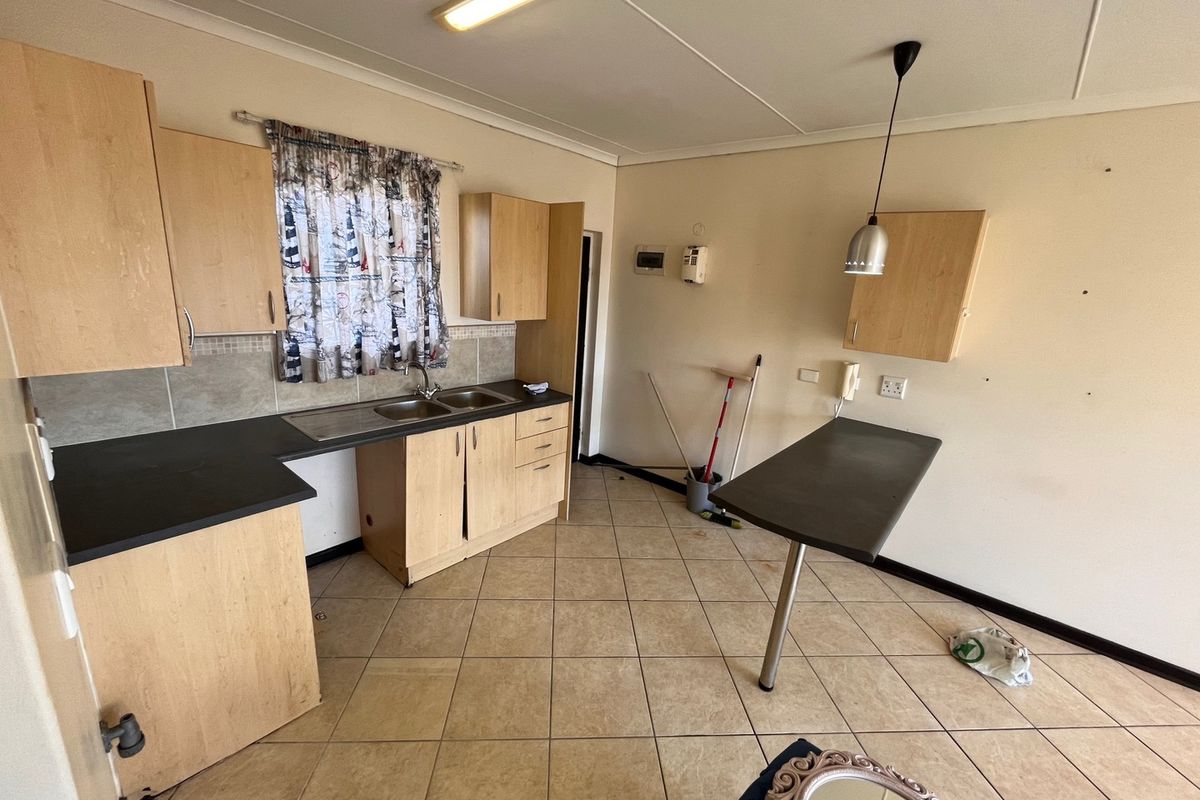 A functional kitchen featuring light wood-tone cabinetry, dark laminate countertops, a double sink, and tiled flooring, offering a blank canvas for potential updates.