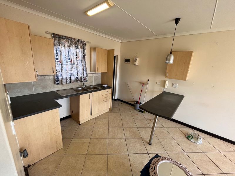 A functional kitchen featuring light wood-tone cabinetry, dark laminate countertops, a double sink, and tiled flooring, offering a blank canvas for potential updates.