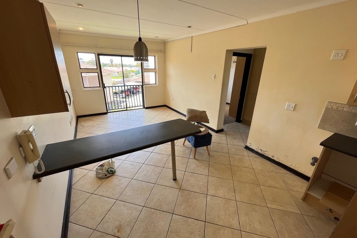Open-plan living area featuring tiled flooring, a breakfast bar, and access to a balcony. The space requires cosmetic attention to wall finishes.