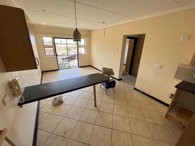 Open-plan living area featuring tiled flooring, a breakfast bar, and access to a balcony. The space requires cosmetic attention to wall finishes.