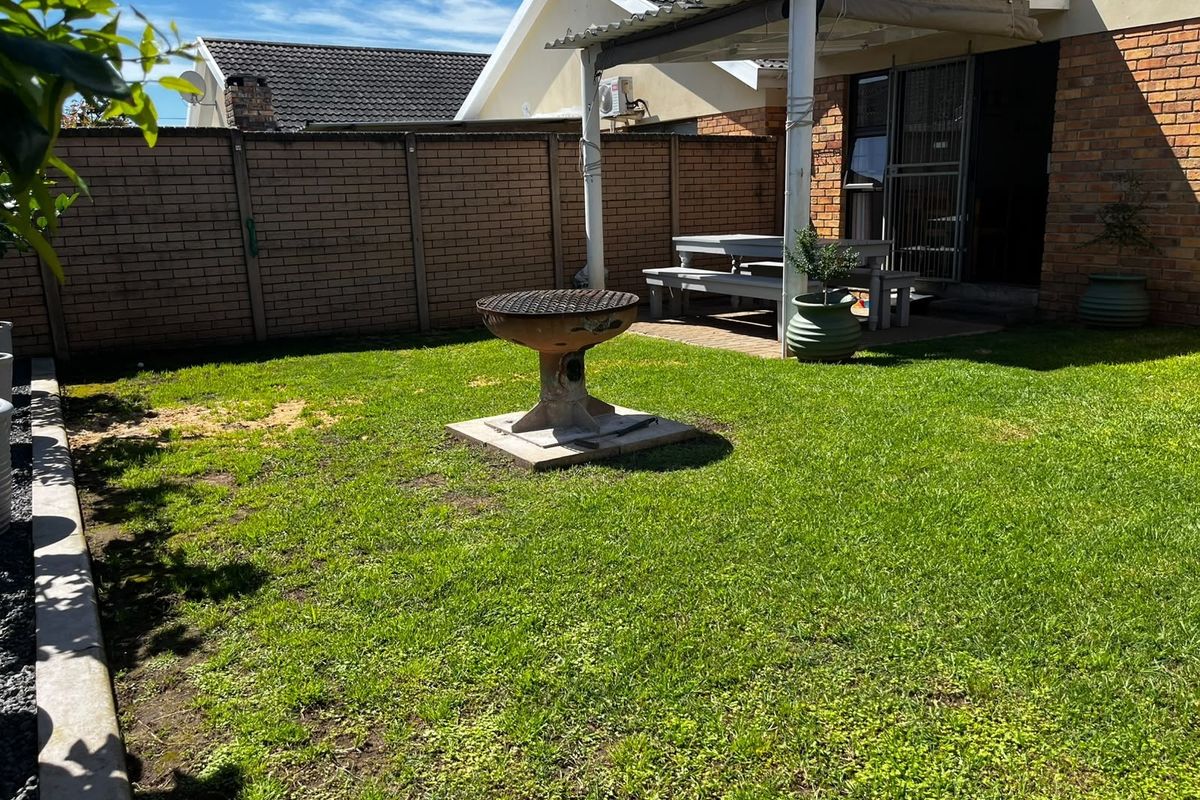 A private rear garden featuring a lawn, a paved covered patio area, and a built-in braai, enclosed by brick boundary walls.