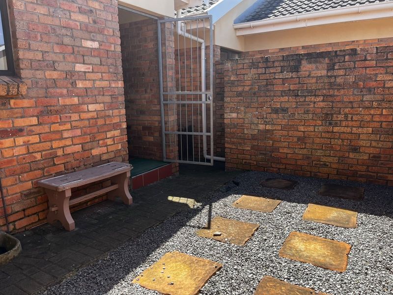 A private rear courtyard featuring brick walls, a security gate, paved sections, and gravel landscaping with stone stepping stones.