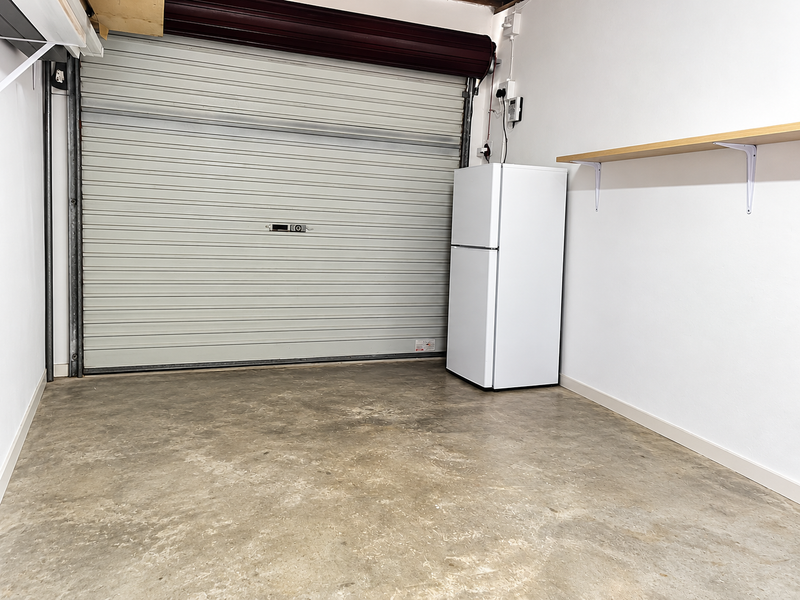 A clean, functional garage space featuring a secure roller door, concrete flooring, and convenient wall-mounted shelving for additional storage.