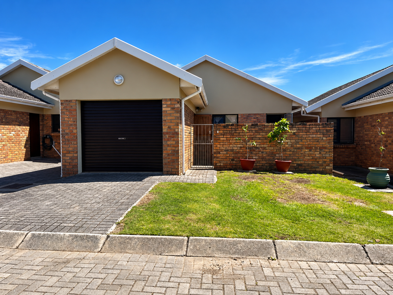Front view of a townhouse featuring a single roller garage door, brick exterior walls, paved driveway, and a small front lawn area.