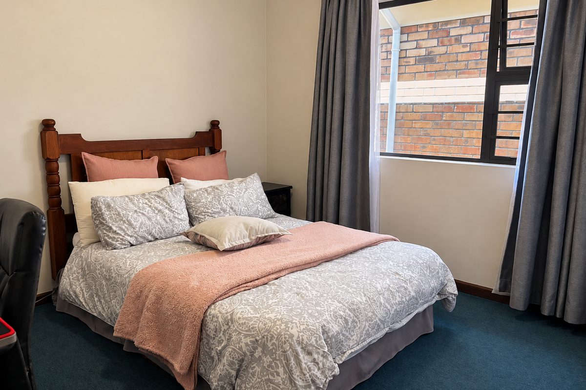A standard bedroom featuring carpeted flooring and an aluminium-framed window with views of an exterior brick wall.