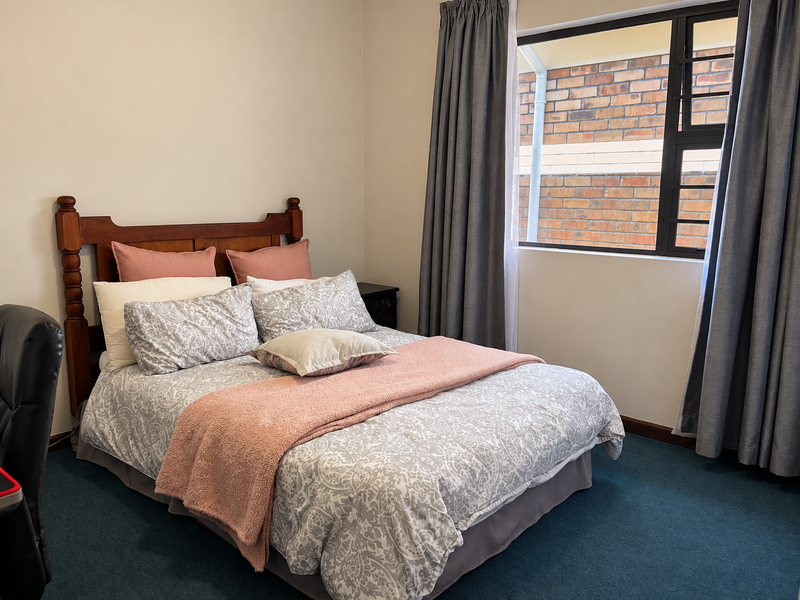 A standard bedroom featuring carpeted flooring and an aluminium-framed window with views of an exterior brick wall.