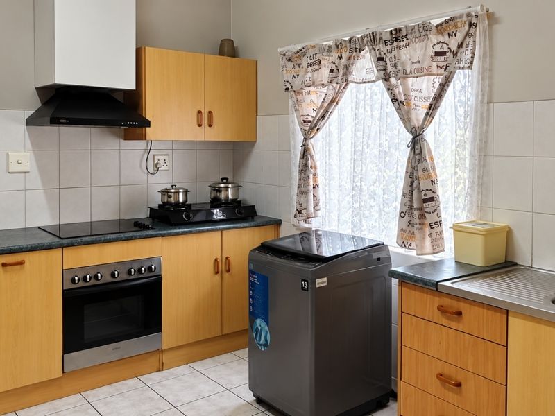 Functional kitchen featuring light wood cabinetry, laminate countertops, built-in oven with extractor fan, and tiled backsplash with neutral floor tiles.