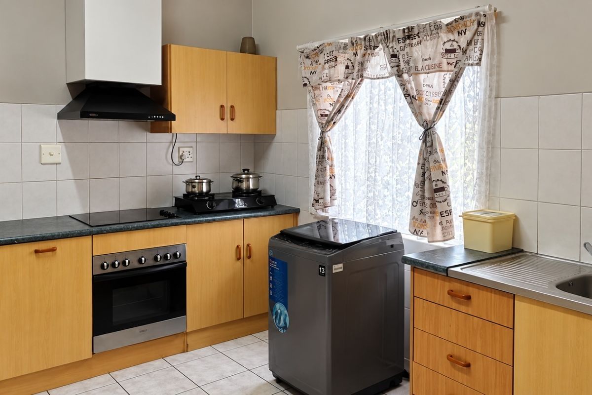 Functional kitchen featuring light wood cabinetry, laminate countertops, built-in oven with extractor fan, and tiled backsplash with neutral floor tiles.