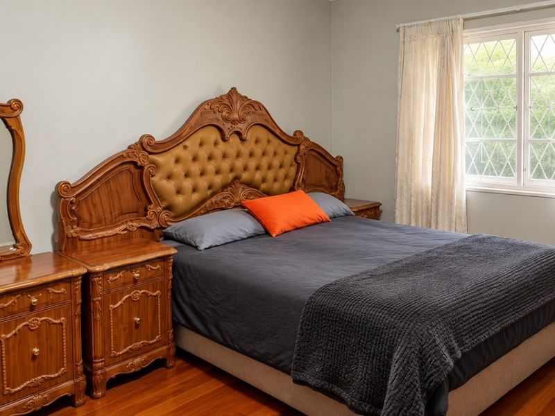 A well-maintained bedroom featuring polished hardwood flooring and a classic leaded glass window with neutral curtains.