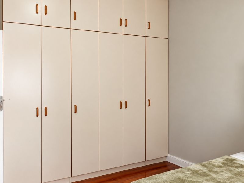 A bedroom featuring extensive floor-to-ceiling built-in cupboards with light-toned cabinetry and polished hardwood flooring.