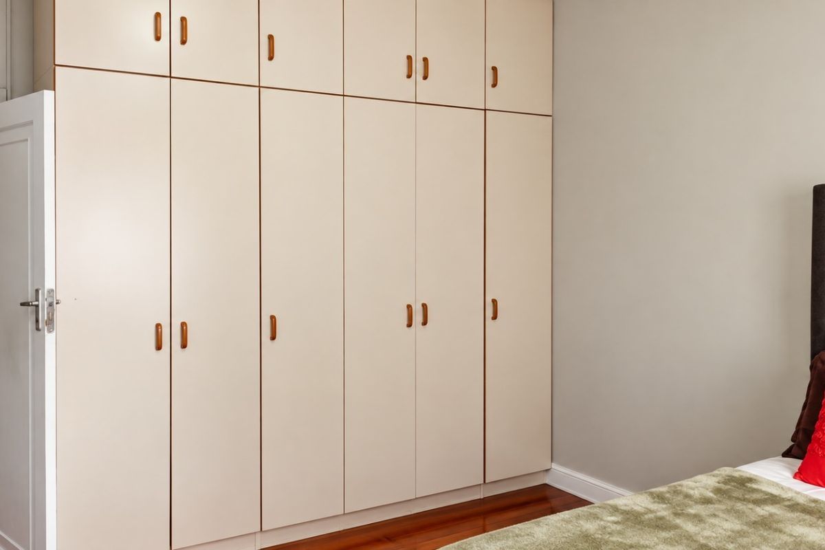 A bedroom featuring extensive floor-to-ceiling built-in cupboards with light-toned cabinetry and polished hardwood flooring.