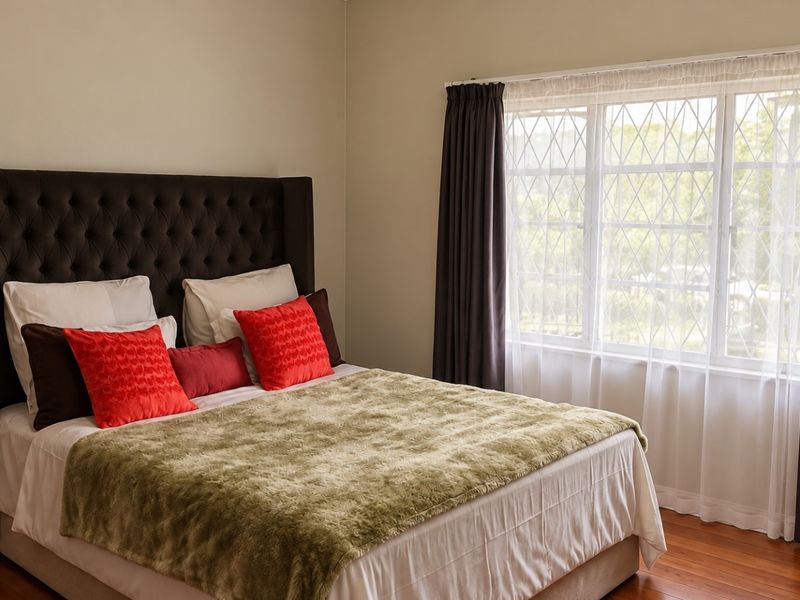 A well-maintained bedroom featuring warm hardwood flooring and a large window with diamond-patterned glazing, providing natural light and a pleasant outlook.