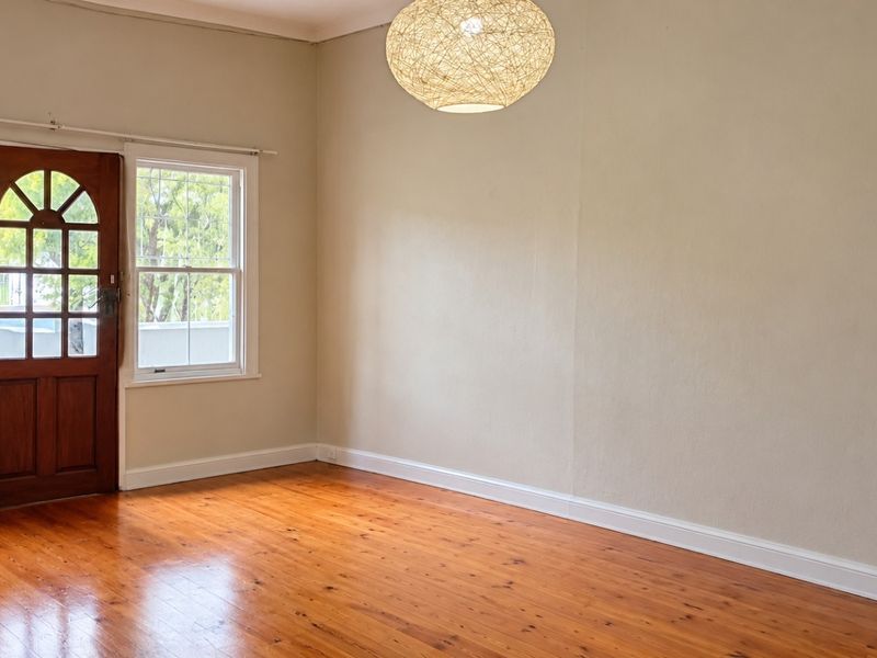 An empty living room featuring polished timber flooring, an arched timber door, and classic sash windows, providing a bright and neutral blank canvas.