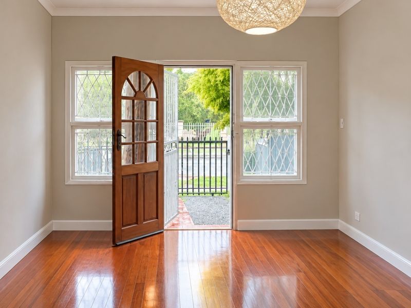 Bright and welcoming entrance area featuring polished timber flooring, a solid timber front door, and secure window treatments.
