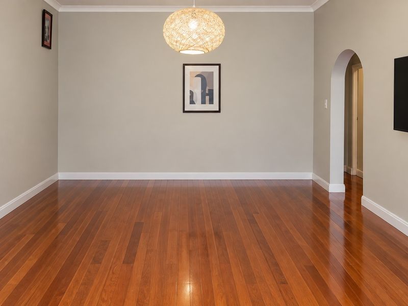 A bright and spacious living room featuring polished hardwood flooring, an elegant arched doorway, and neutral wall tones.