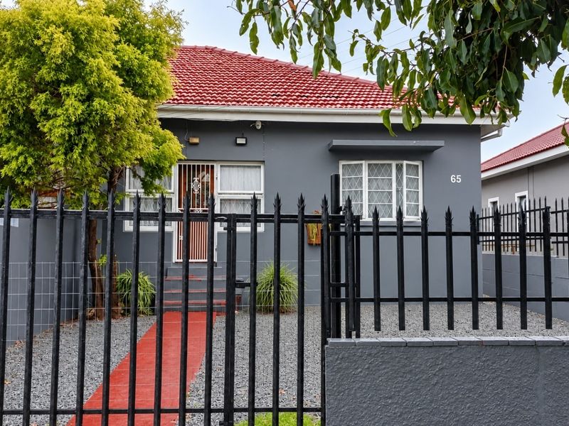 Front elevation of a single-story house featuring a grey facade, red tiled roof, and secure metal fencing with a gated entrance.