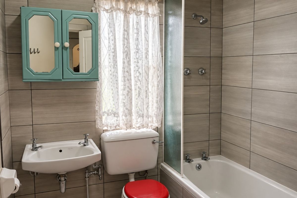 A functional bathroom featuring tiled walls, a wall-mounted basin, a toilet, and a bathtub with a glass shower screen.