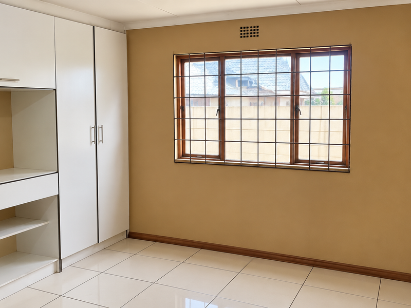 A clean, empty bedroom featuring neutral walls, tiled flooring, and a white built-in wardrobe with integrated shelving.