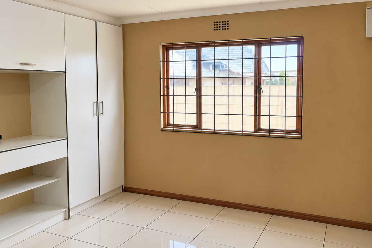 A clean, empty bedroom featuring neutral walls, tiled flooring, and a white built-in wardrobe with integrated shelving.