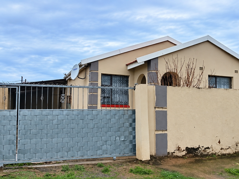 Front view of a single-story house featuring a sliding metal gate, perimeter wall with security bars, and a tiled roof.